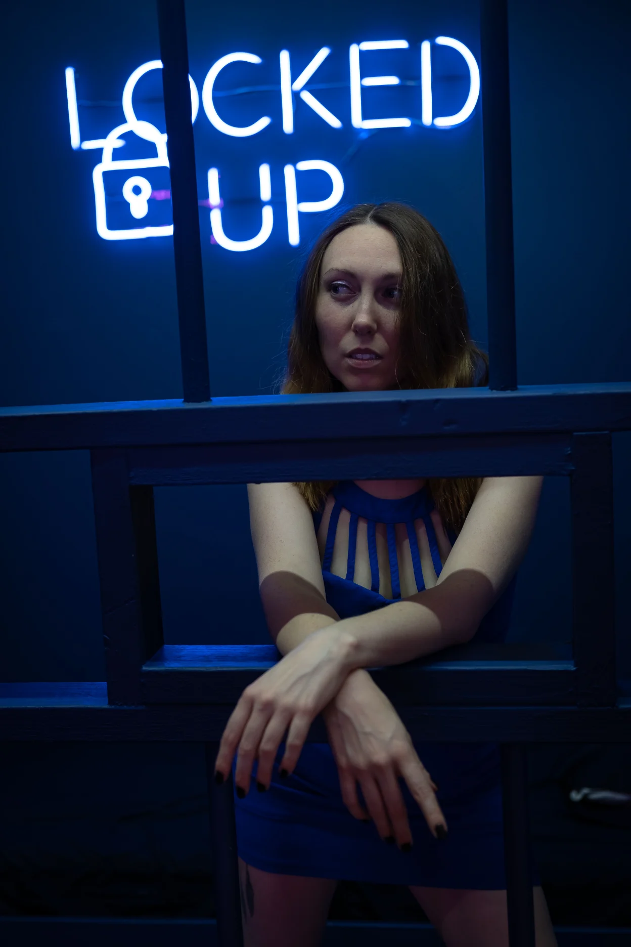 Person behind bars under a Locked Up neon sign